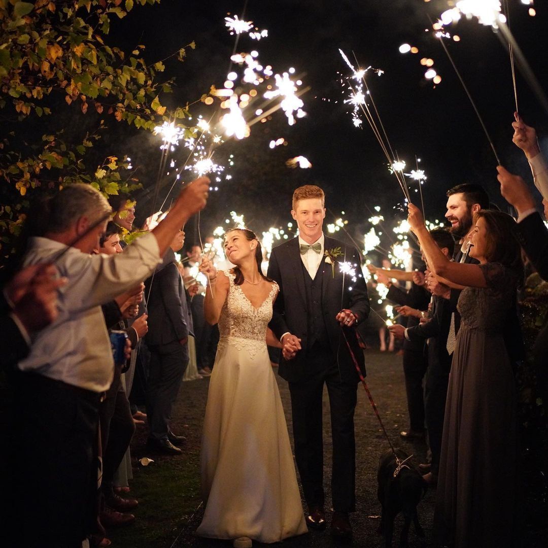 A bride and groom are walking through a crowd of people holding sparklers