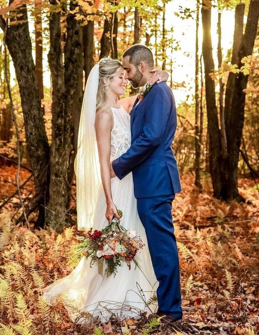 A bride and groom are kissing in the woods.