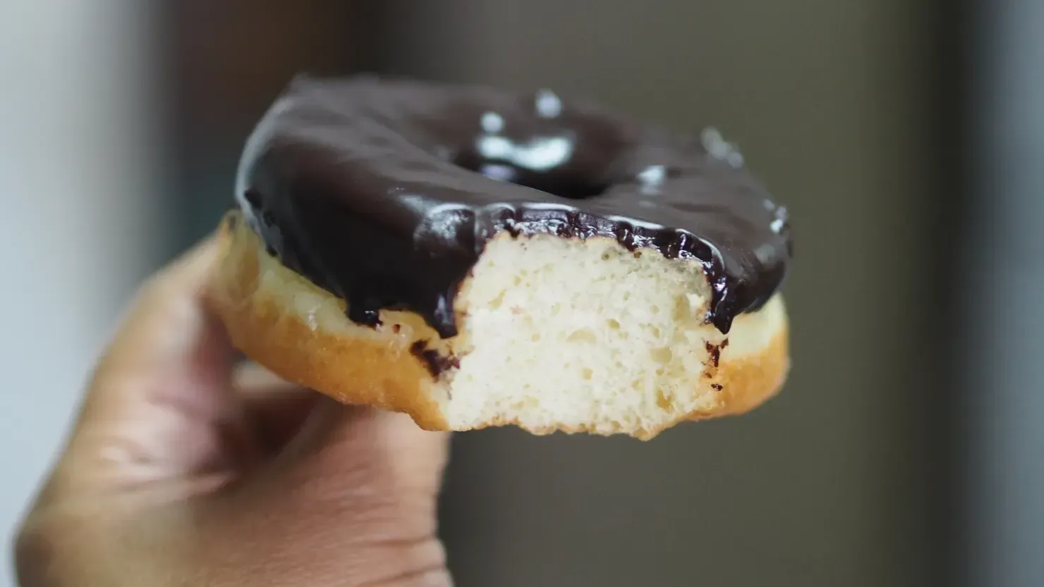 Hand die een met chocolade besmeerde donut vasthoudt, de kruimels aan de binnenkant zijn zichtbaar.