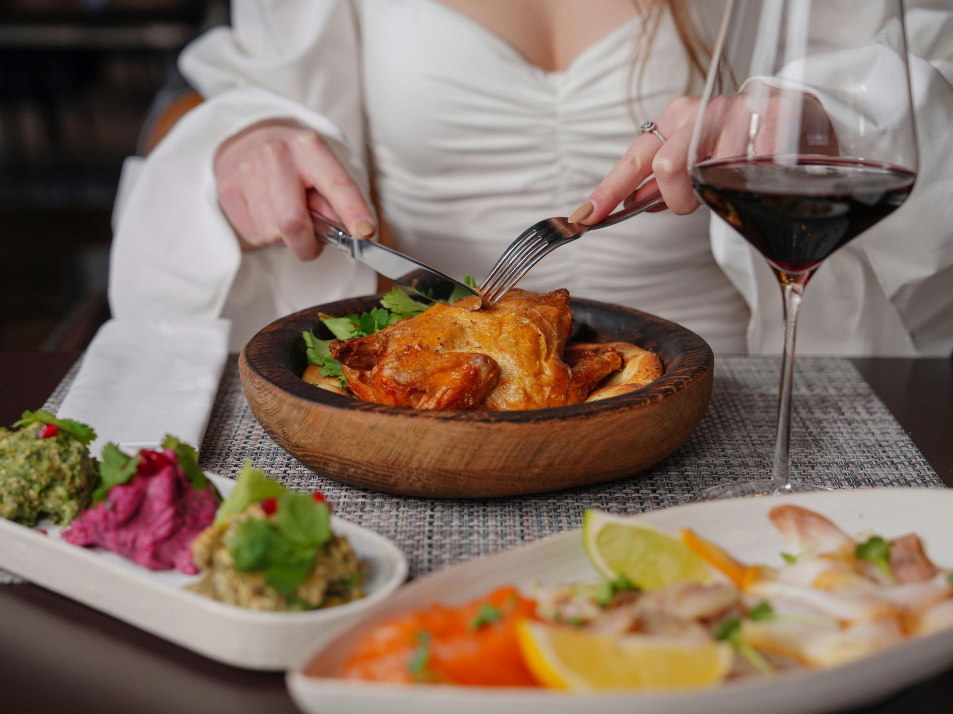 A woman is sitting at a table eating food and drinking wine.