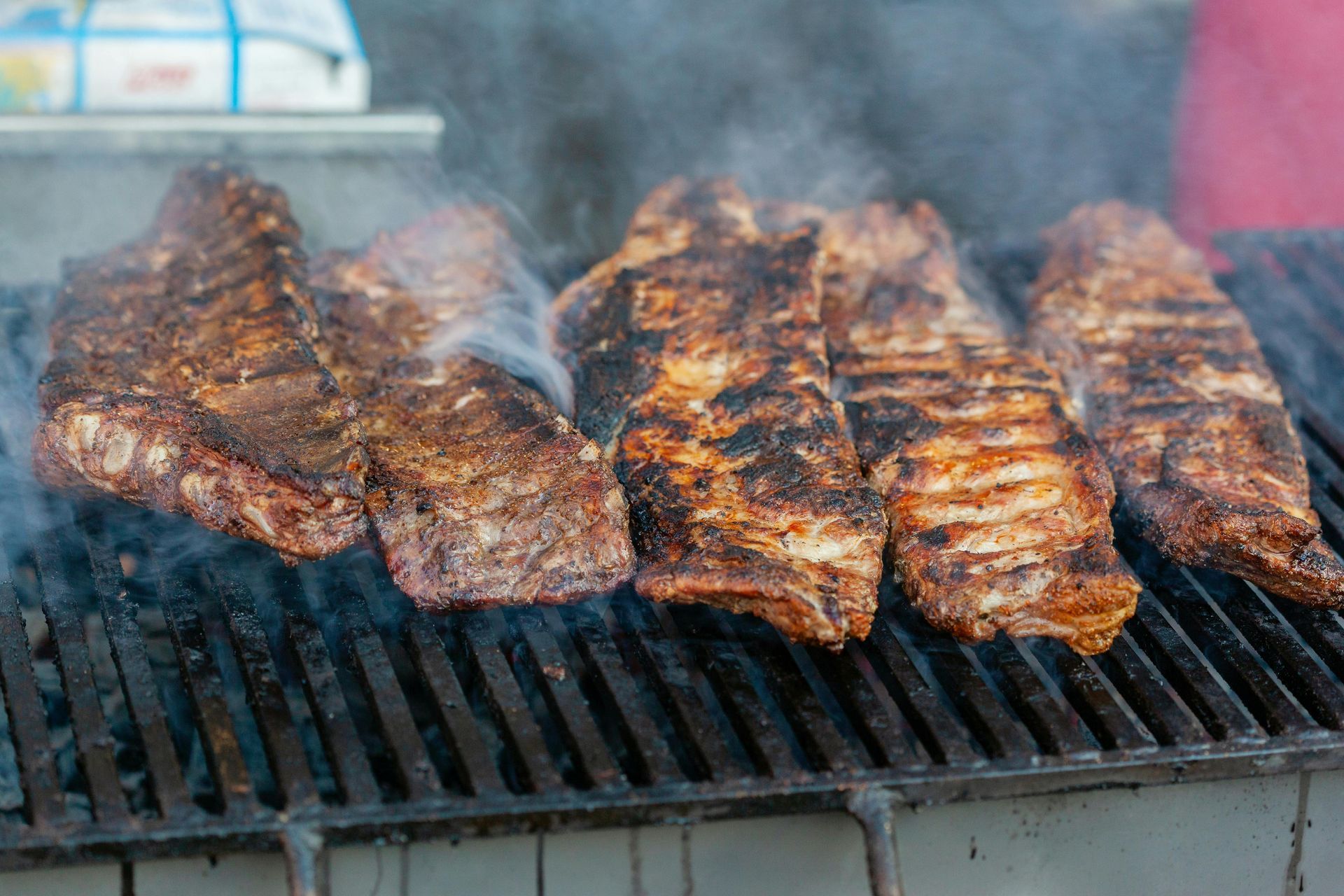 Ribs are cooking on a grill with smoke coming out of them.