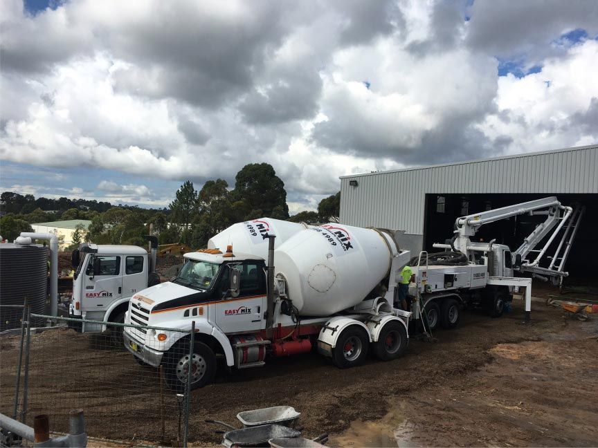 Concrete Mixer Trucks Parked Near a Building Under a Cloudy Sky — Easy Mix Concrete in Berkeley Vale, NSW