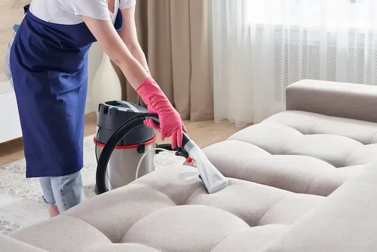 A woman is cleaning a couch with a vacuum cleaner.