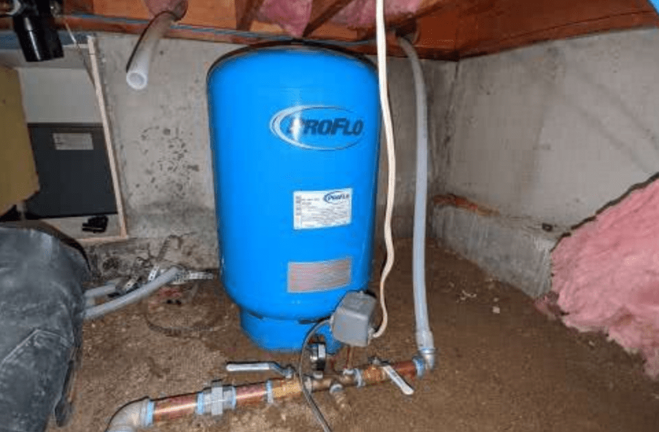A blue water tank is sitting under a ceiling in a basement.