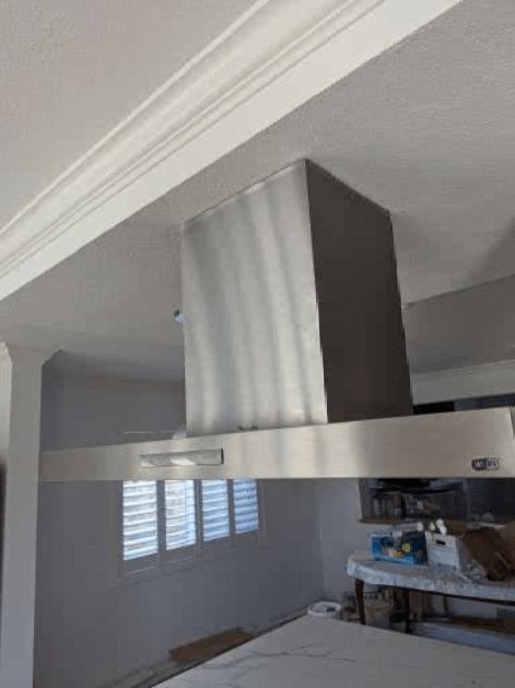 A stainless steel hood is hanging from the ceiling in a kitchen.