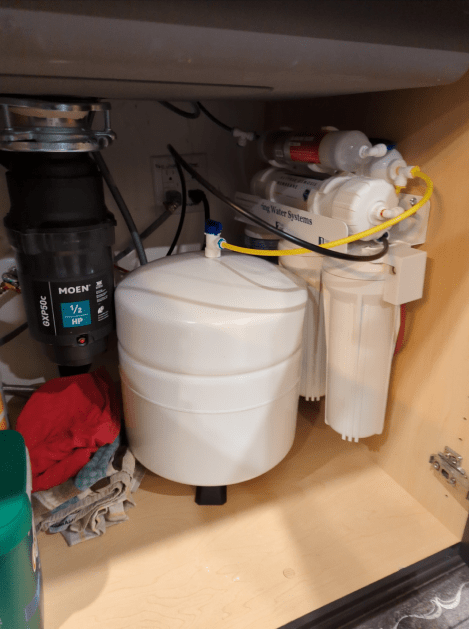 A water filter is sitting under a sink in a kitchen.