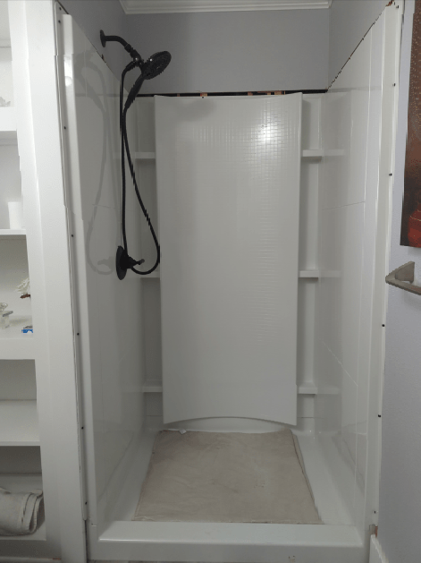 A shower stall with a shower head and shelves in a bathroom.