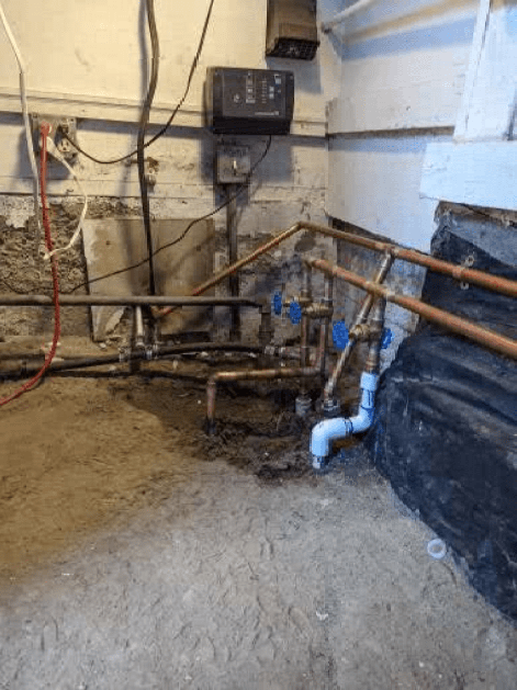 A dirty basement with a lot of pipes and wires.