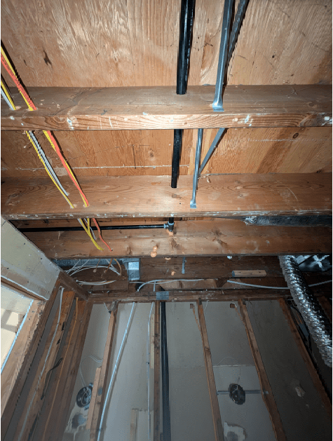The ceiling of a room with wooden beams and wires.