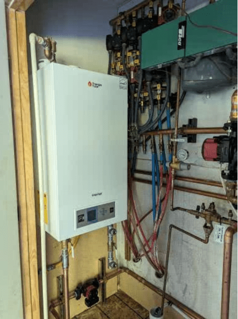 A white boiler is sitting in a room surrounded by pipes
