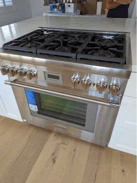 A stainless steel stove top oven is sitting on top of a wooden floor in a kitchen.