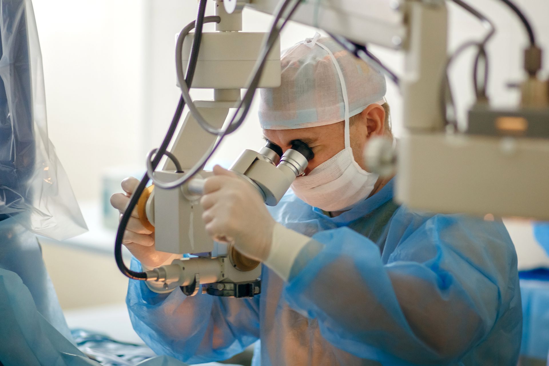 A surgeon using an ophthalmic microscope during a delicate eye procedure in a sterile operating room