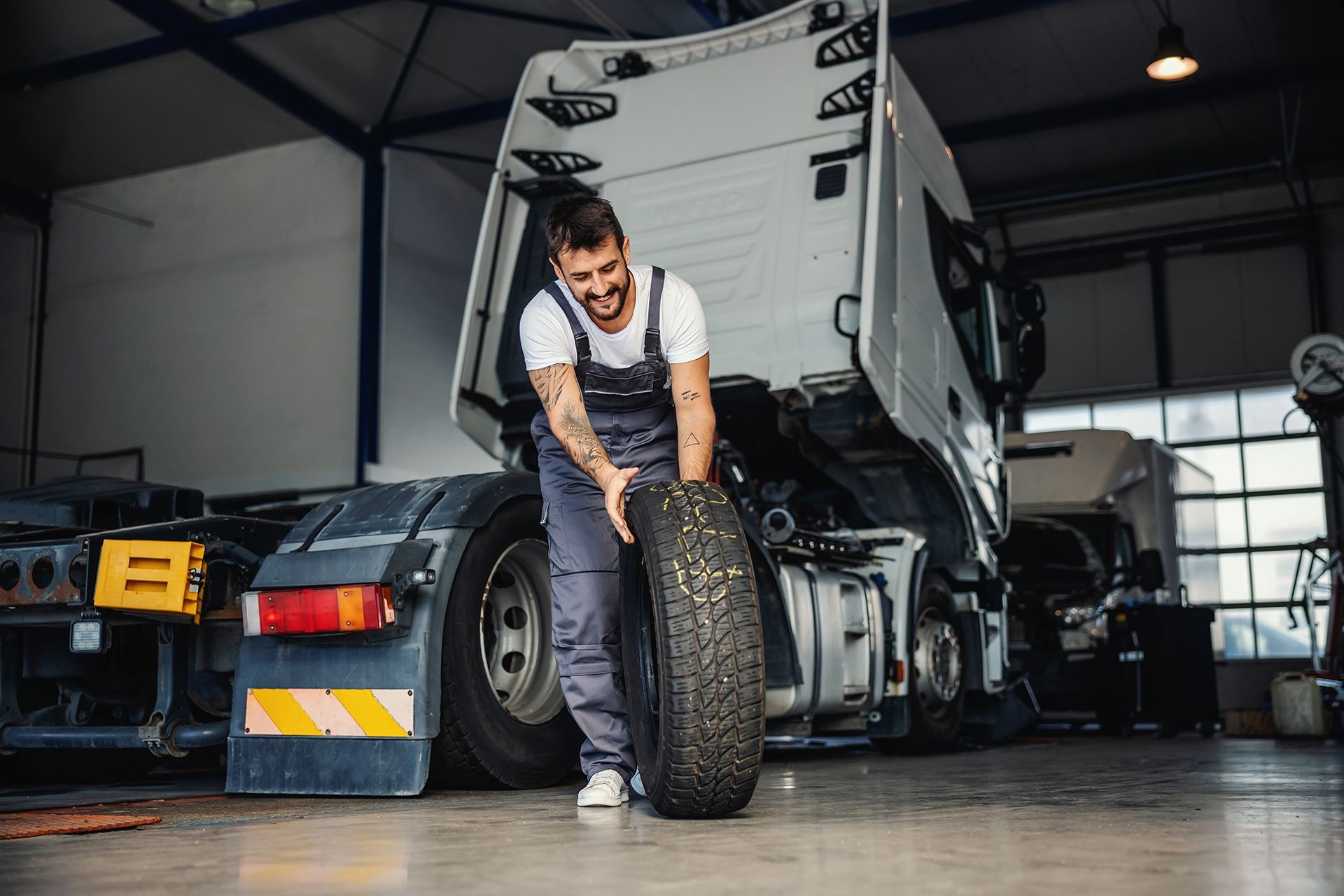 A man is changing a tire on a truck in a garage.