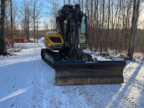 A yellow and black excavator is parked on a snowy road.