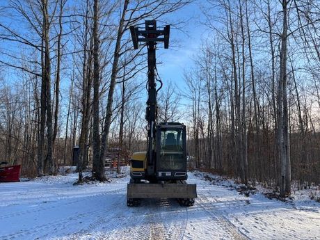 A small excavator with fork lift is parked on a snowy road in the woods.