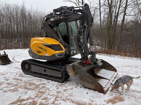 A yellow and black excavator is parked in the snow next to a dog.