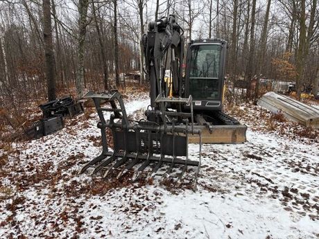 A small excavator is parked in the snow in the woods.