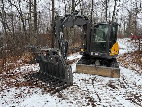 A small excavator is parked on a snowy road next to a tree.