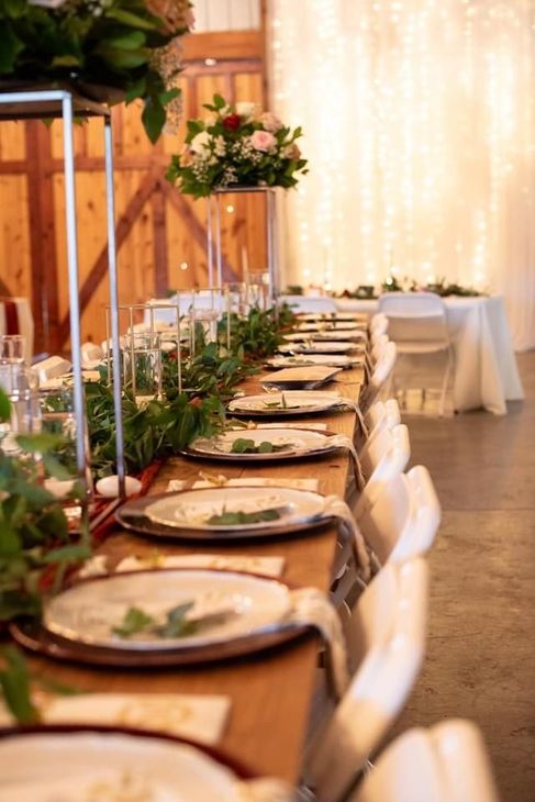 Elegant long banquet table with white chairs, gold tableware, and floral centerpieces in a warmly lit room