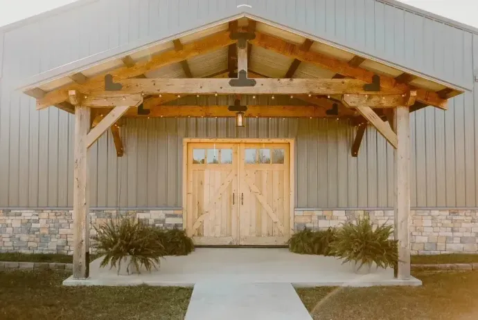 Wooden barn-style building entrance with double doors, stone base, and a concrete walkway under a small porch