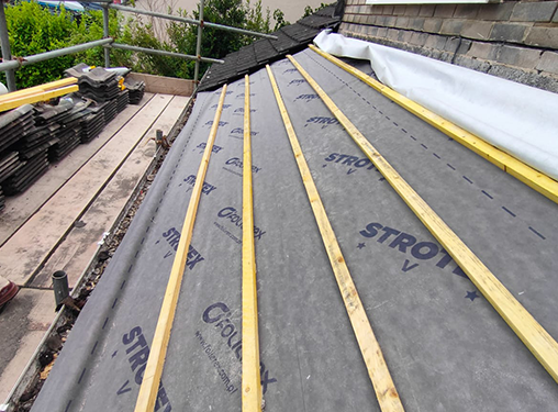 The roof of a house is being covered with styrofoam and wooden beams.