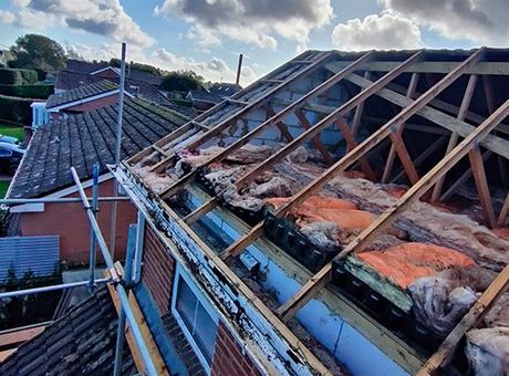 The roof of a house is being built with wooden beams and insulation.