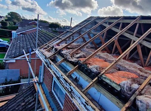 The roof of a house is being remodeled with wooden beams and insulation.