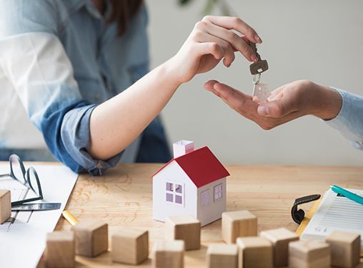 A woman is handing a key to a man in front of a model house.