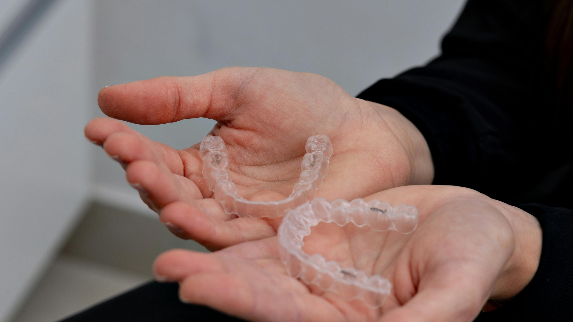 A person is holding two clear braces in their hands.