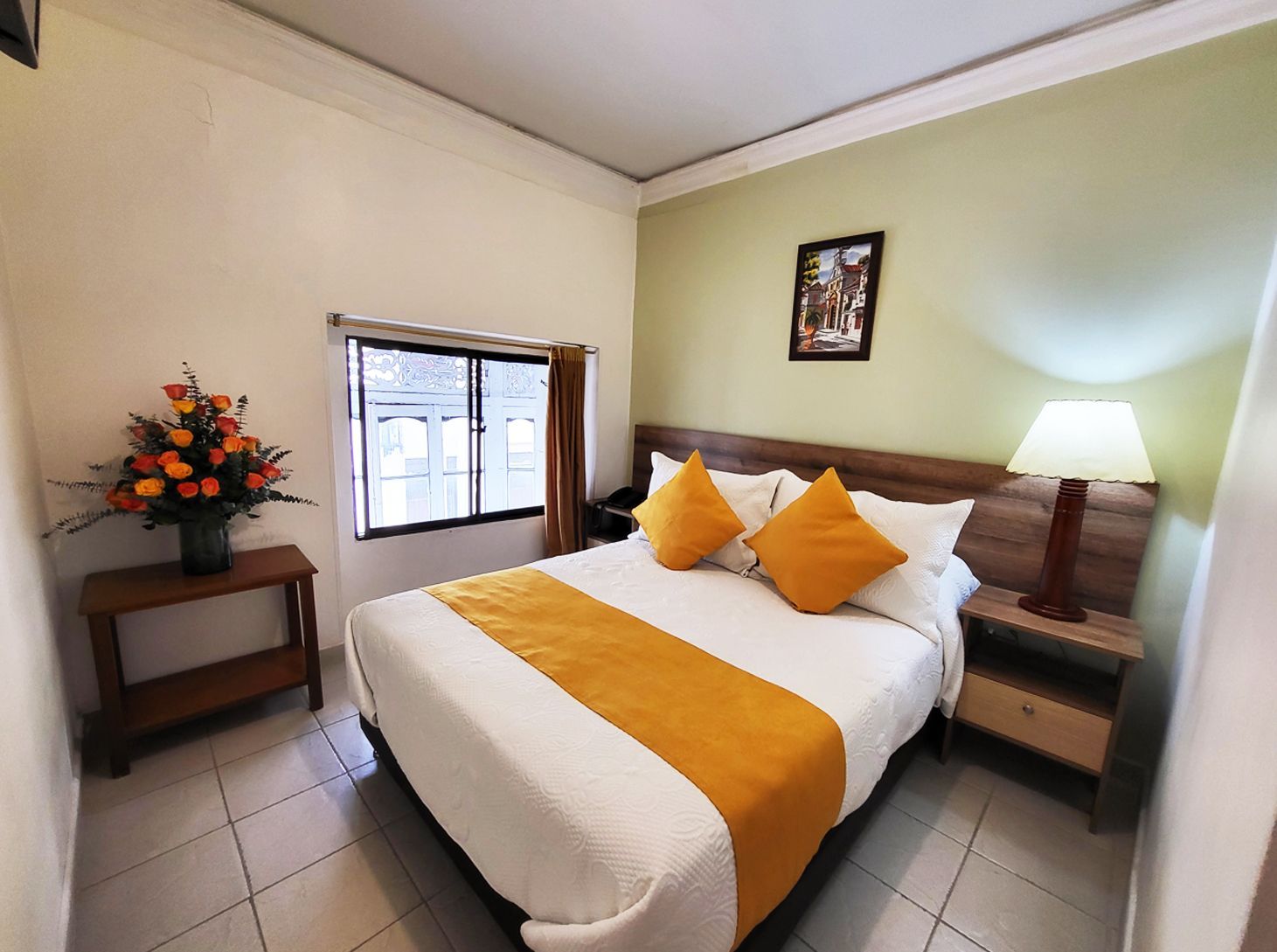 Bedroom with double bed, orange accents, wooden furniture, window, and a floral arrangement.