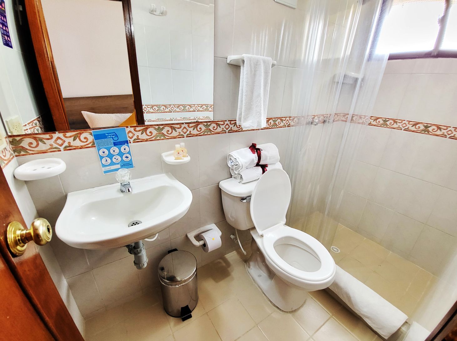 Small bathroom with a white toilet, sink, and shower area. Brown trim, and a mirror.