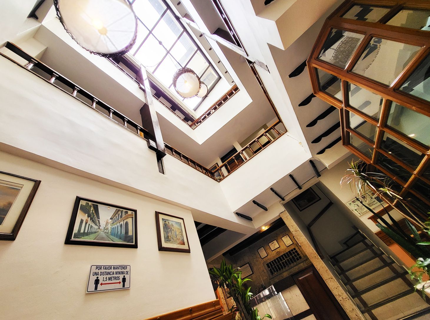 Interior view looking up through a multi-story building with a skylight. White walls, artwork, and a staircase are visible.