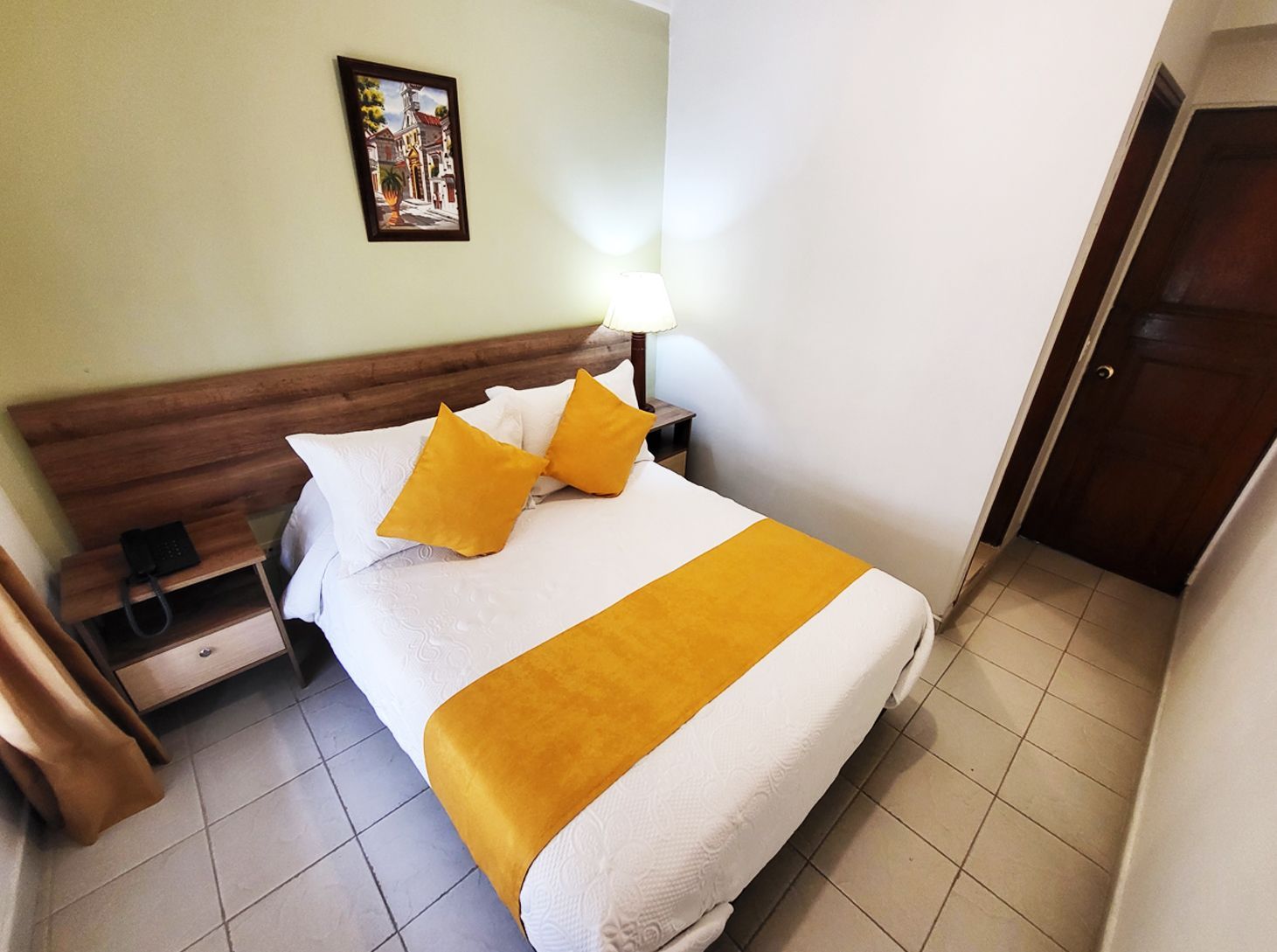 Hotel room with double bed, yellow accents, artwork, and a closed door.