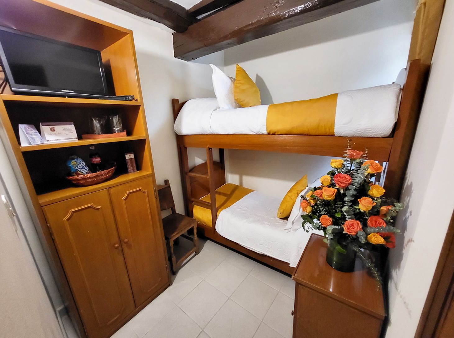 Wooden bunk beds in a small room with a TV cabinet, side table, and a vase of flowers.