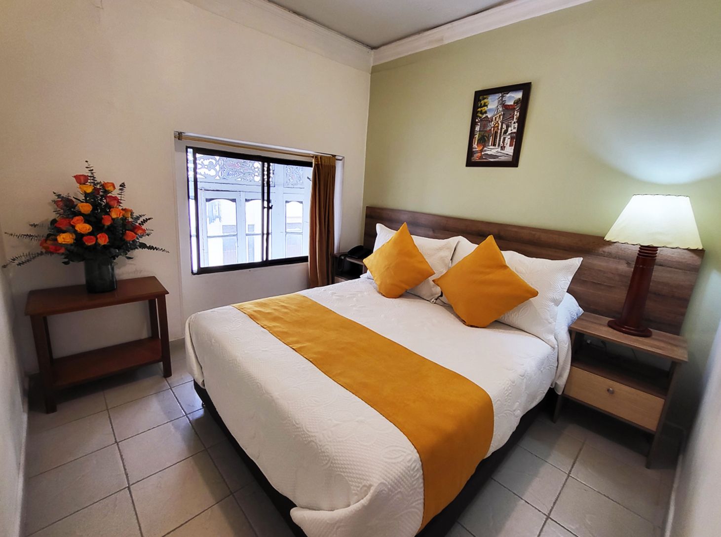 Bedroom with a bed, nightstand, window, and flowers. Yellow and white bedding, light green wall.