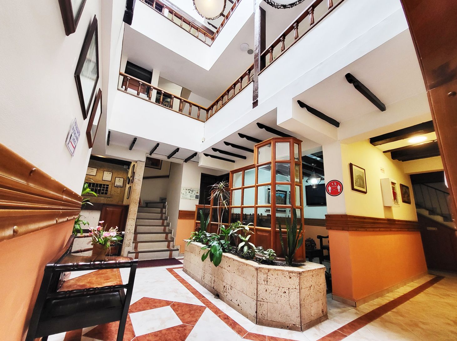 Interior view of a multi-story building with a central courtyard, featuring a staircase, balconies, and potted plants.