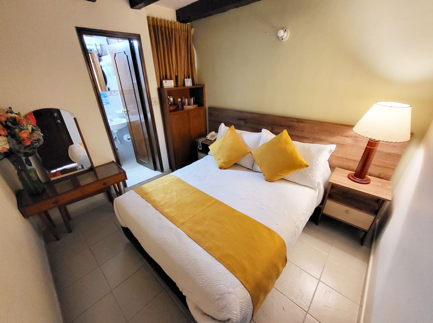Small hotel room with a bed, dresser, lamp, and a doorway to a bathroom.