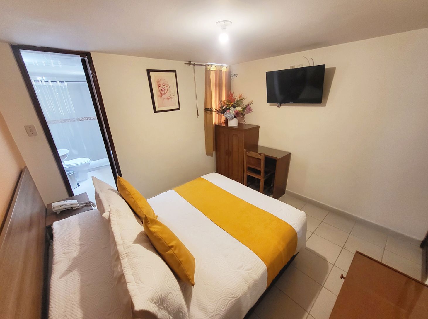 Hotel room with bed, TV, wooden furniture, and a bathroom door.