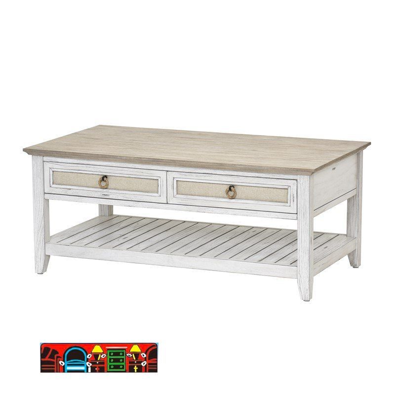 The Captiva Island cocktail table features a coastal design with a distressed white and beach sand finish. It includes two drawers with outdoor fabric fronts, woven knobs, and a lower shelf.