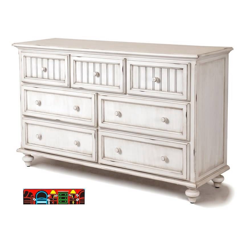 The Monaco Triple Dresser features solid wood construction with a distressed white finish, turned feet, and seven drawers.