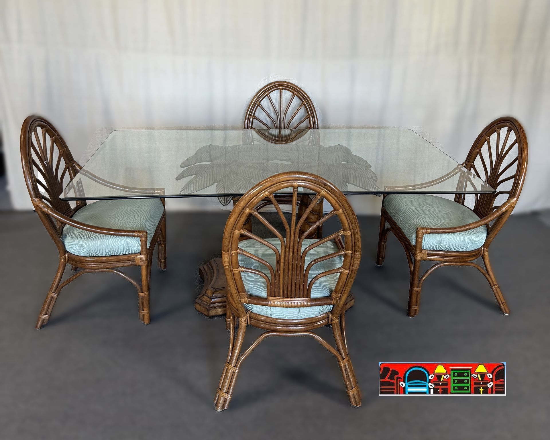 'A gently used five-piece dining set featuring a rectangular glass table with a palm tree-designed base and four rattan armchairs in brown, complemented by blue upholstered seats.'
