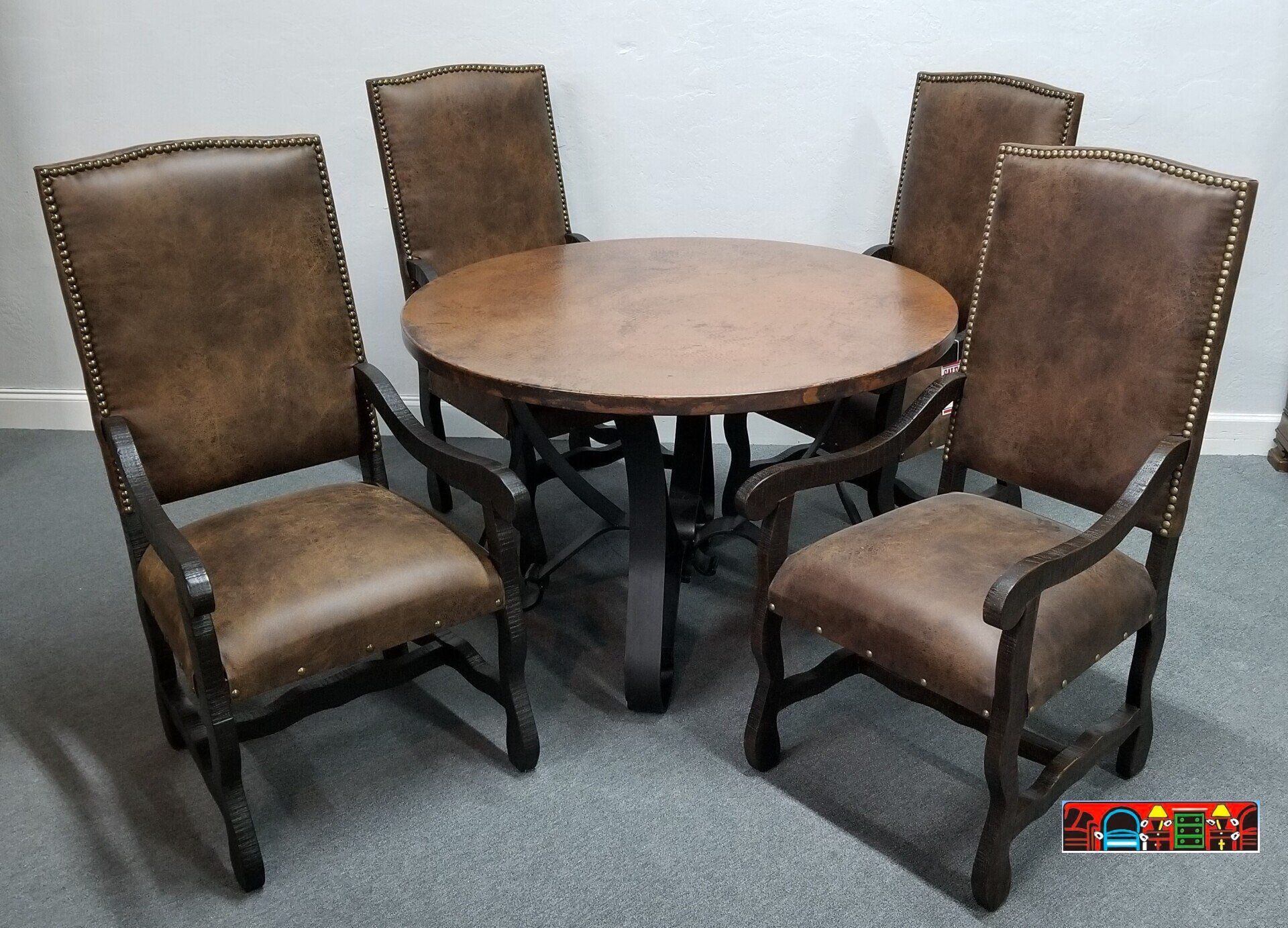 Handcrafted round copper-topped table with a black flat-iron base, accompanied by four exposed wood armchairs in dark brown, featuring medium brown cushions with nail head accents.