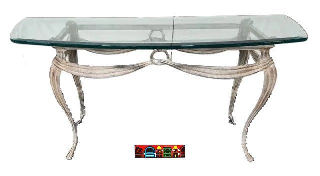A gently used console table featuring an iron frame and beveled glass in beige, adorned with a decorative swooping iron apron and supported by four elegantly curved legs.