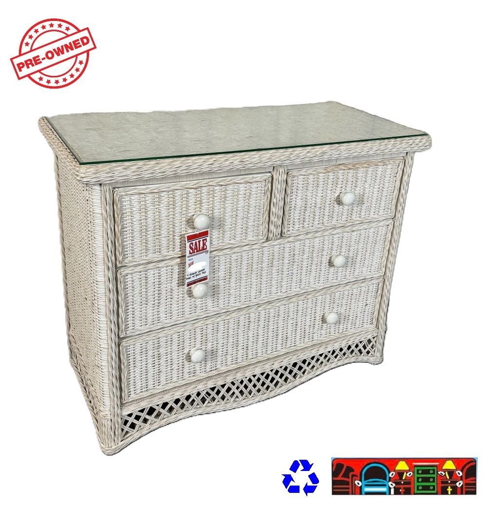 A bedroom chest with four drawers made of whitewashed wicker, a glass top and a lattice bottom.