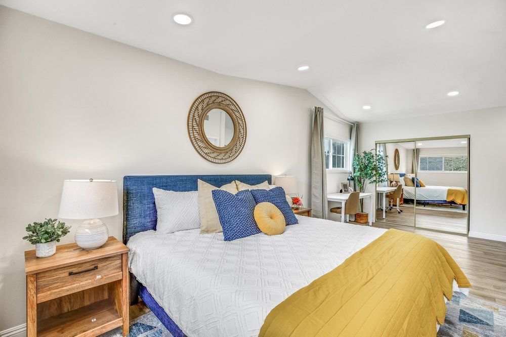 A bedroom with a bed , nightstand , lamp and mirror.