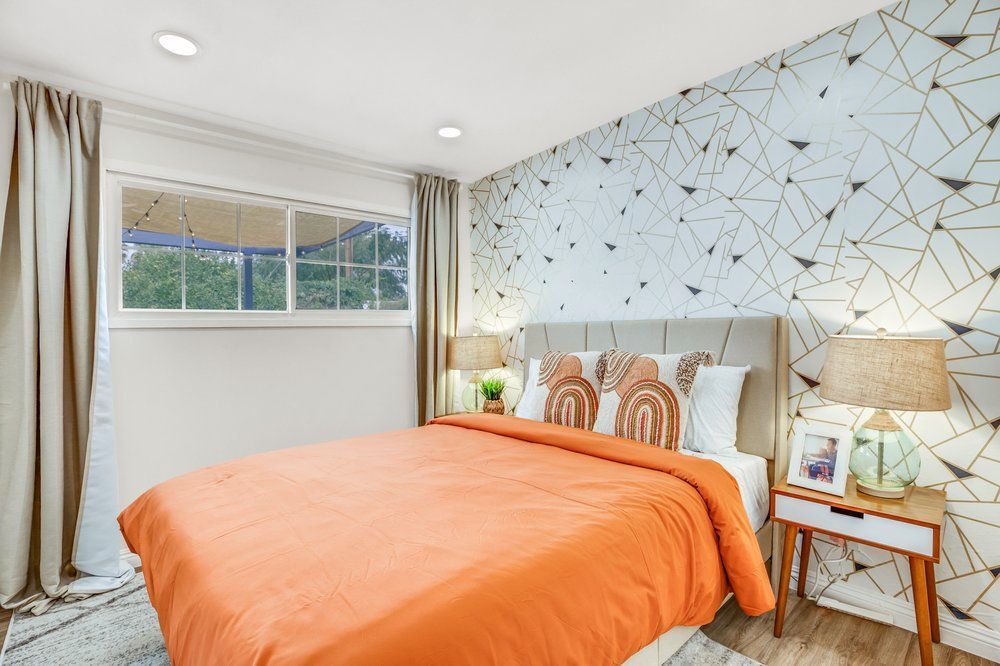 A bedroom with a bed , nightstand , lamps and a window.