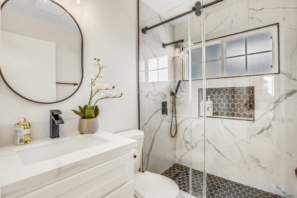 A bathroom with a toilet , sink , mirror and walk in shower.