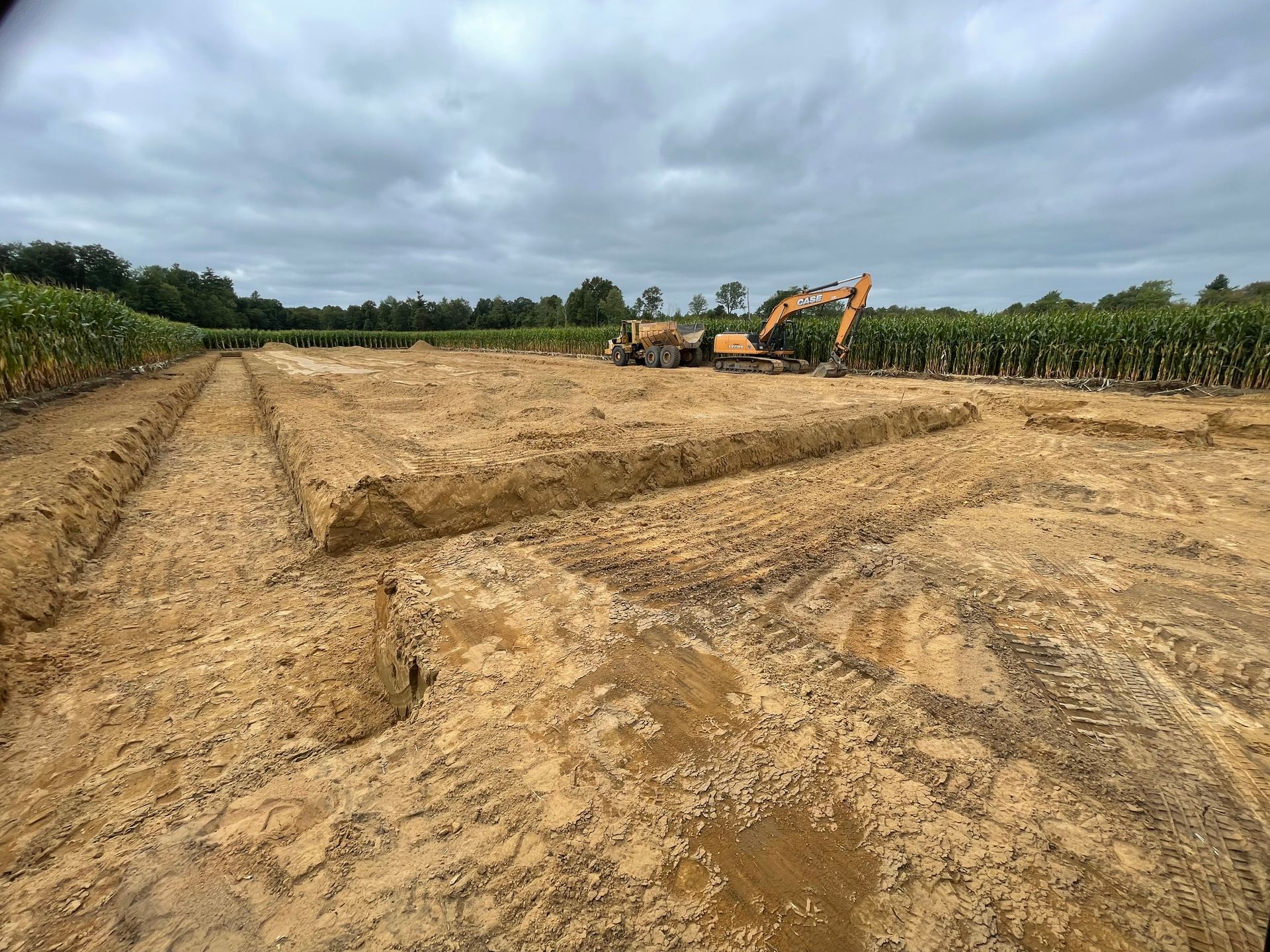 Excavator beside field preparing footing and foundation for new barn building.