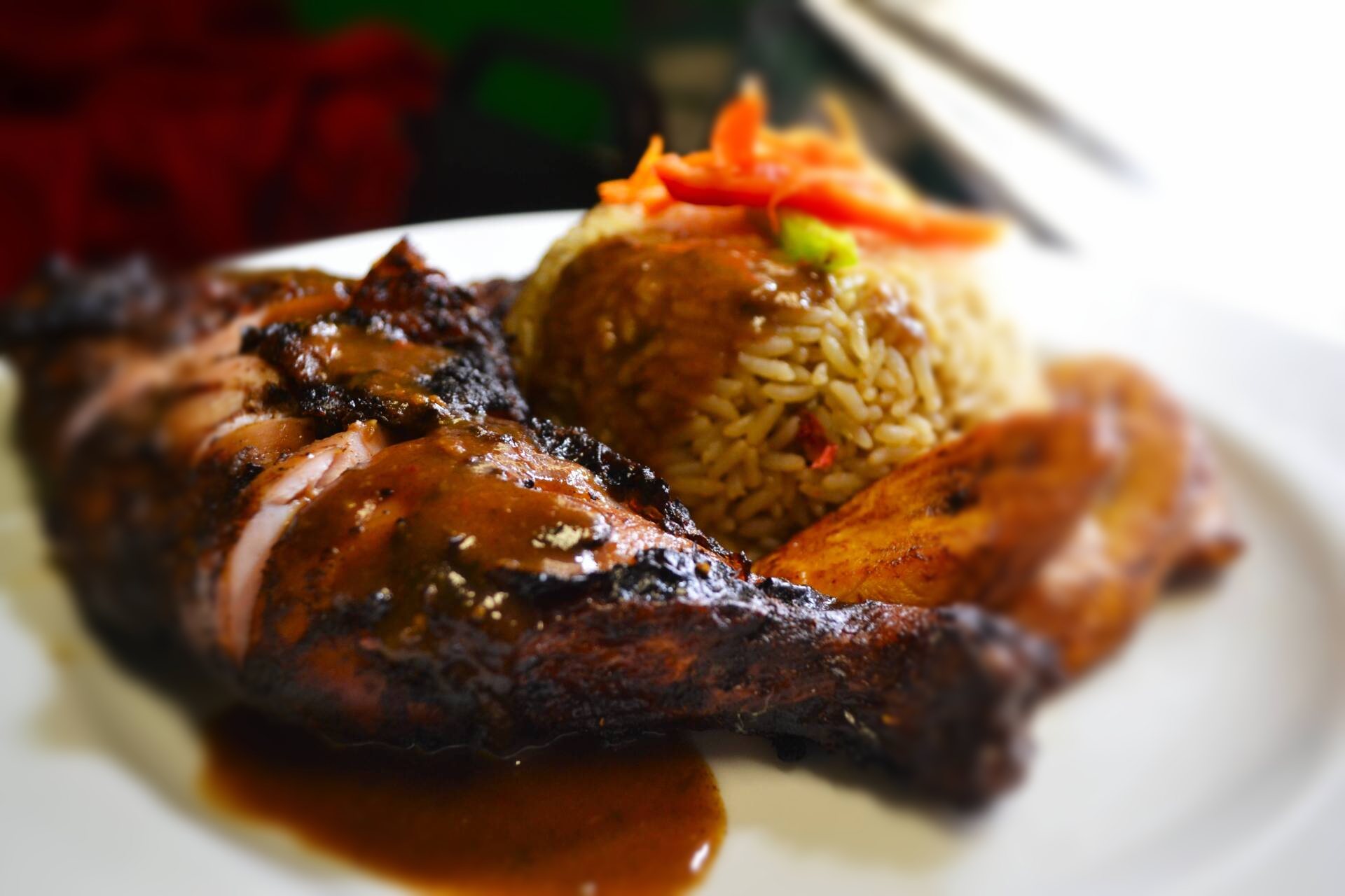 A white plate topped with Jerk Chicken, Rice and Peas and Plantain