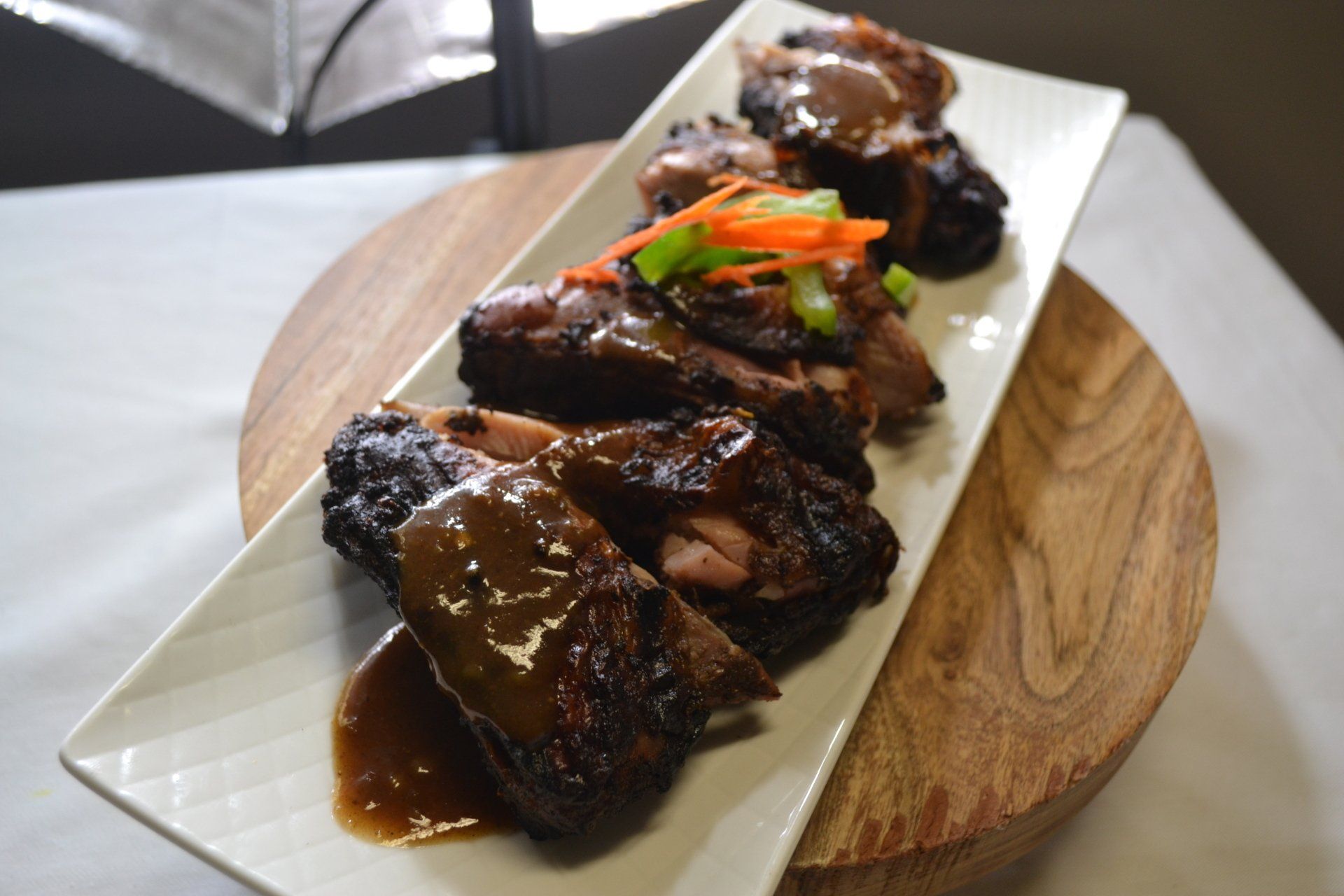 A white plate topped with meat and sauce on a wooden cutting board